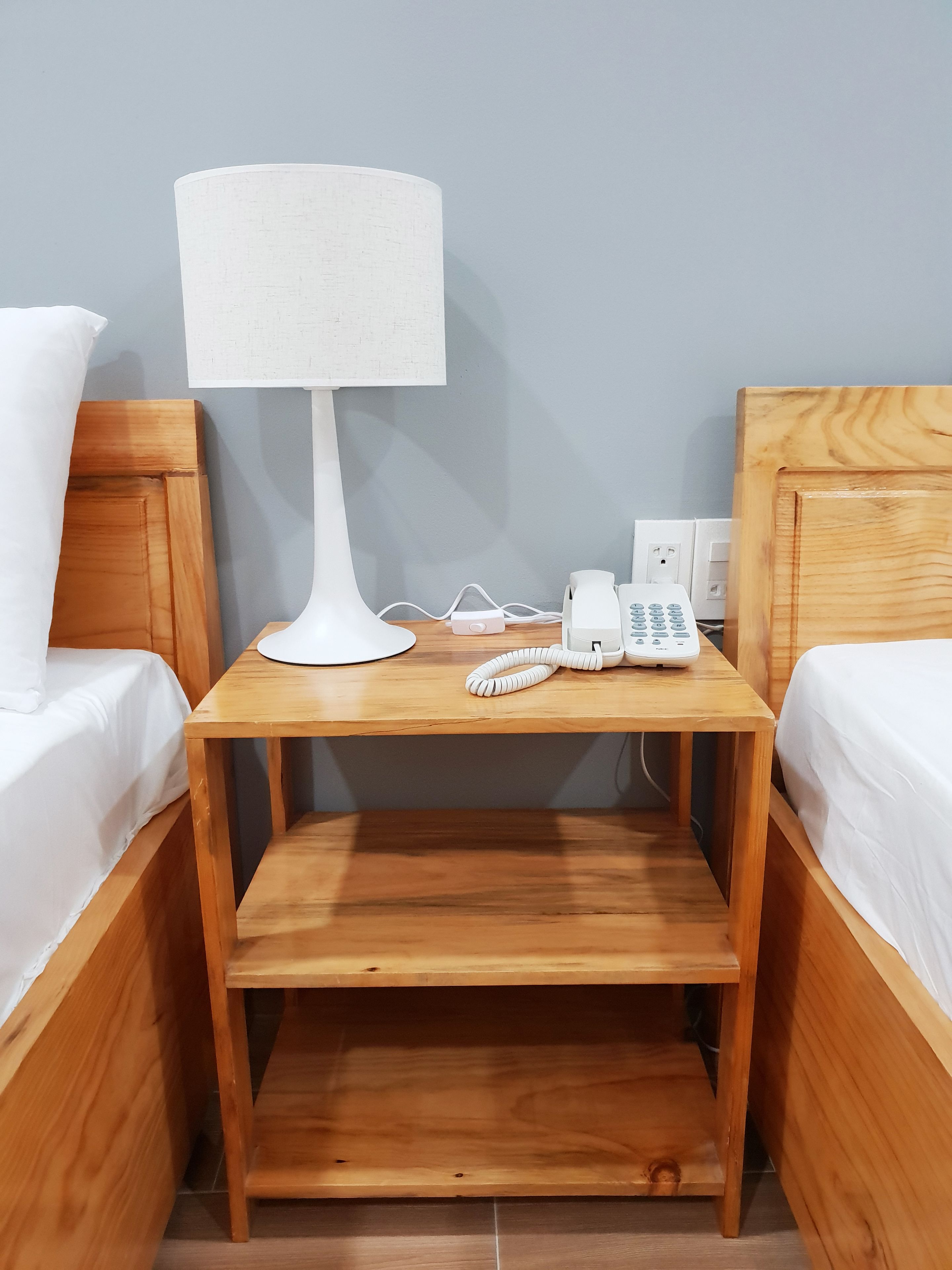 A small wooden nightstand with a white lamp, a telephone, and a power strip.