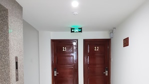 A hallway with two wooden doors labeled 2.1 and 2.2, a green exit sign, and a white tiled floor. - Khách sạn Quy Nhơn Center (Quy Nhon)