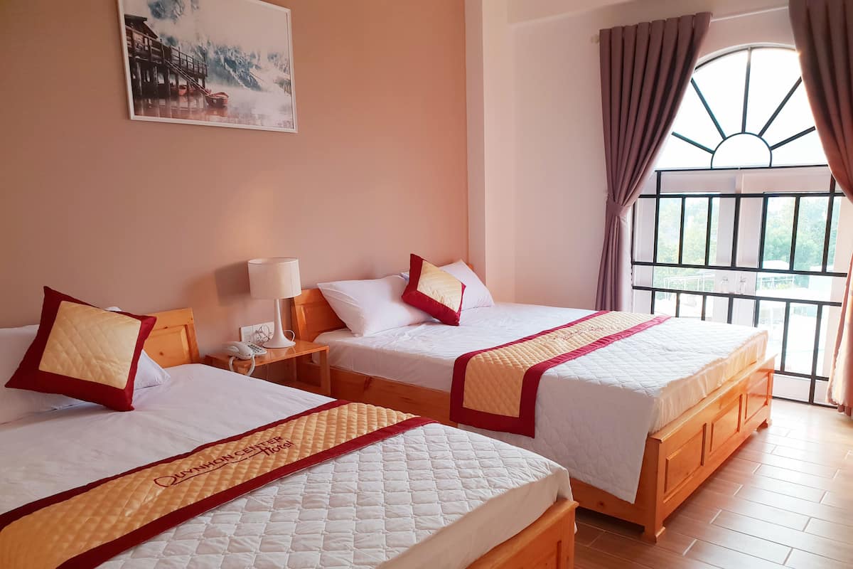 Two double beds with wooden frames and white bedding, a bedside table with a lamp, and a painting on the wall.