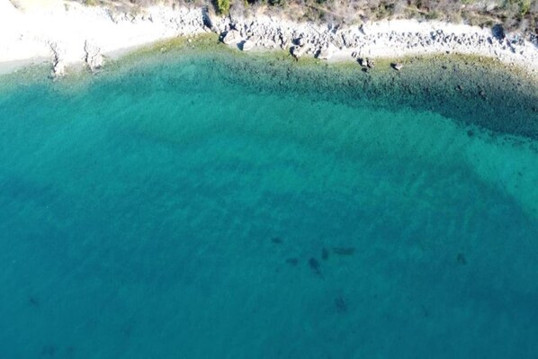 Vista aérea de una playa con aguas turquesas cristalinas y un litoral rocoso.