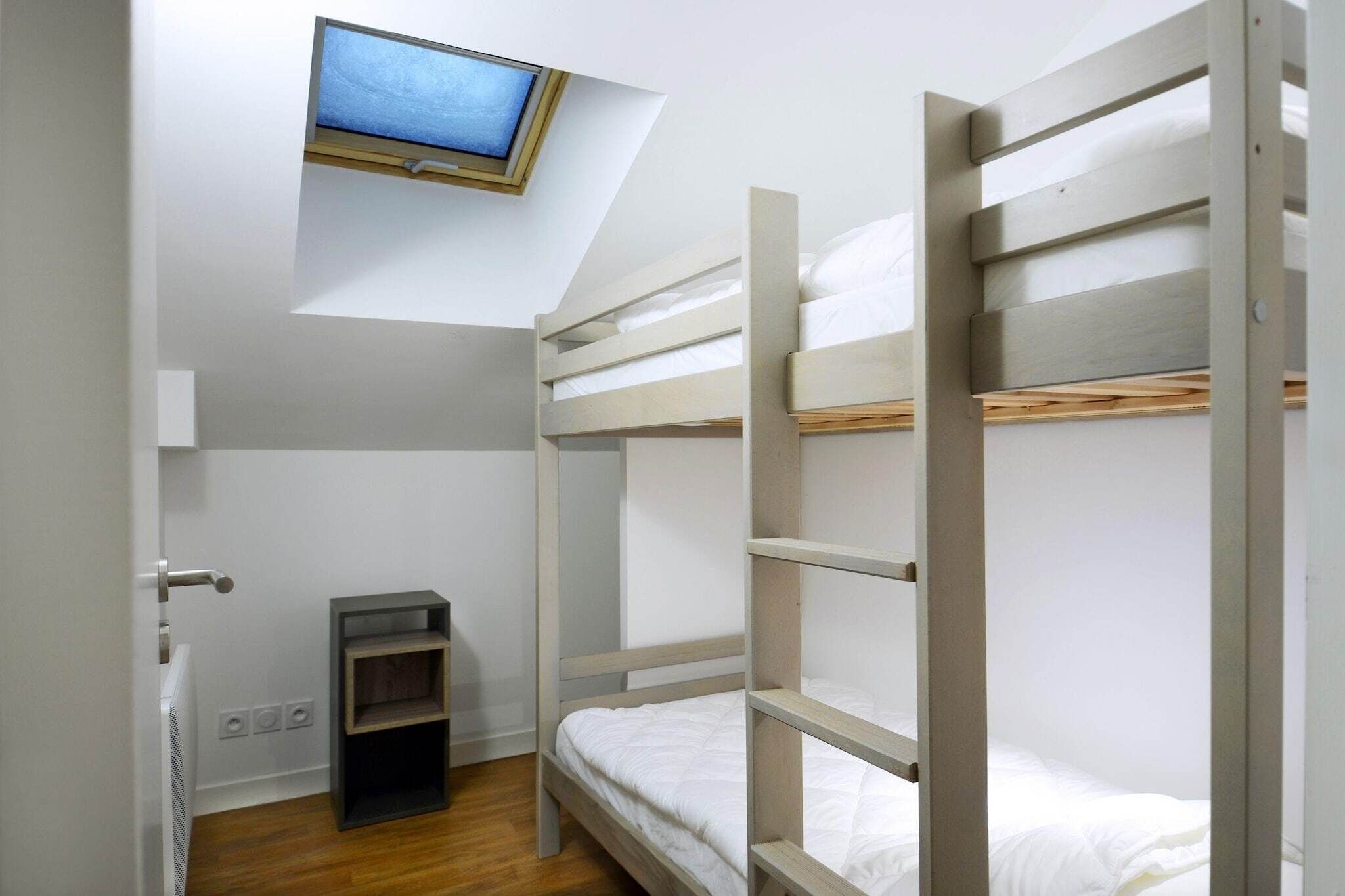 A bunk bed room with a television above the headboard, a small shelf, and a door.