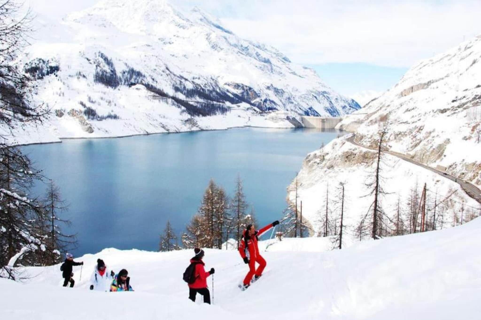 A group of people skiing on a snowy mountain slope with a lake and mountains in the background.