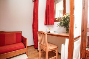 A small room with a wooden desk, a red sofa, a chair, and a window with red curtains.