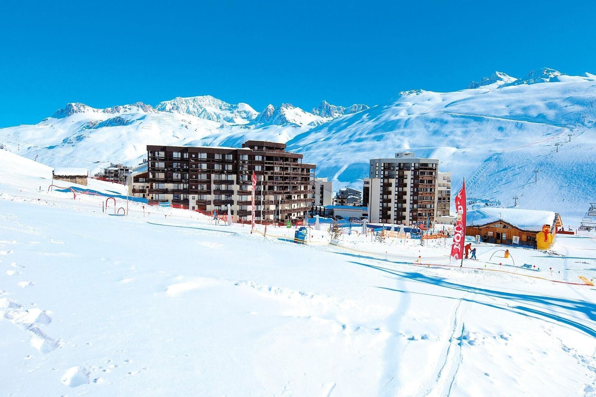 A snow-covered mountain town with modern buildings, ski slopes, and a clear blue sky.
