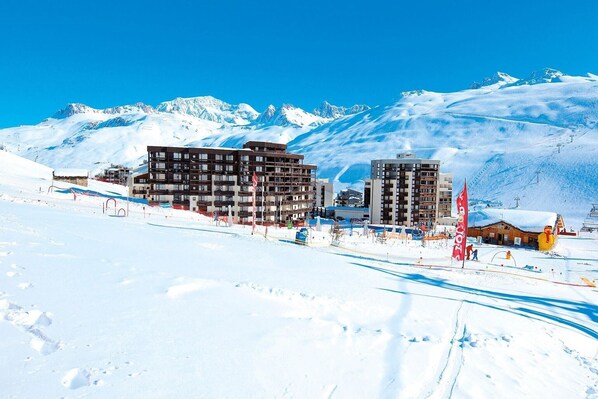 A snow-covered mountain town with modern buildings, ski slopes, and a clear blue sky.