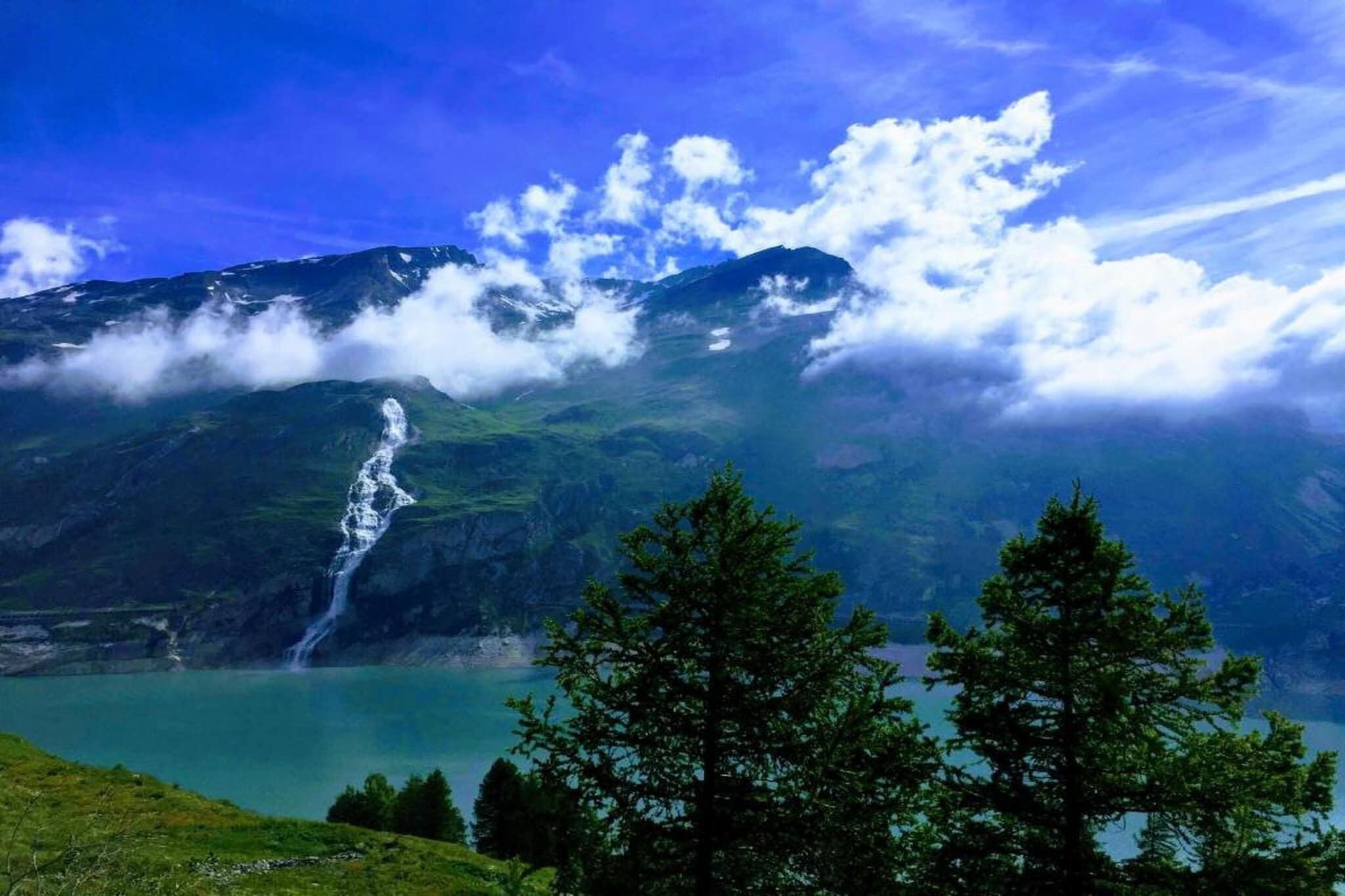 A mountainous landscape with a waterfall, a lake, and a forested area.