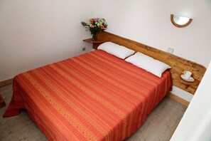 Ein Bett mit rotem, gemustertem Bettbezug, weißen Kissen und einem hölzernen Kopfteil.