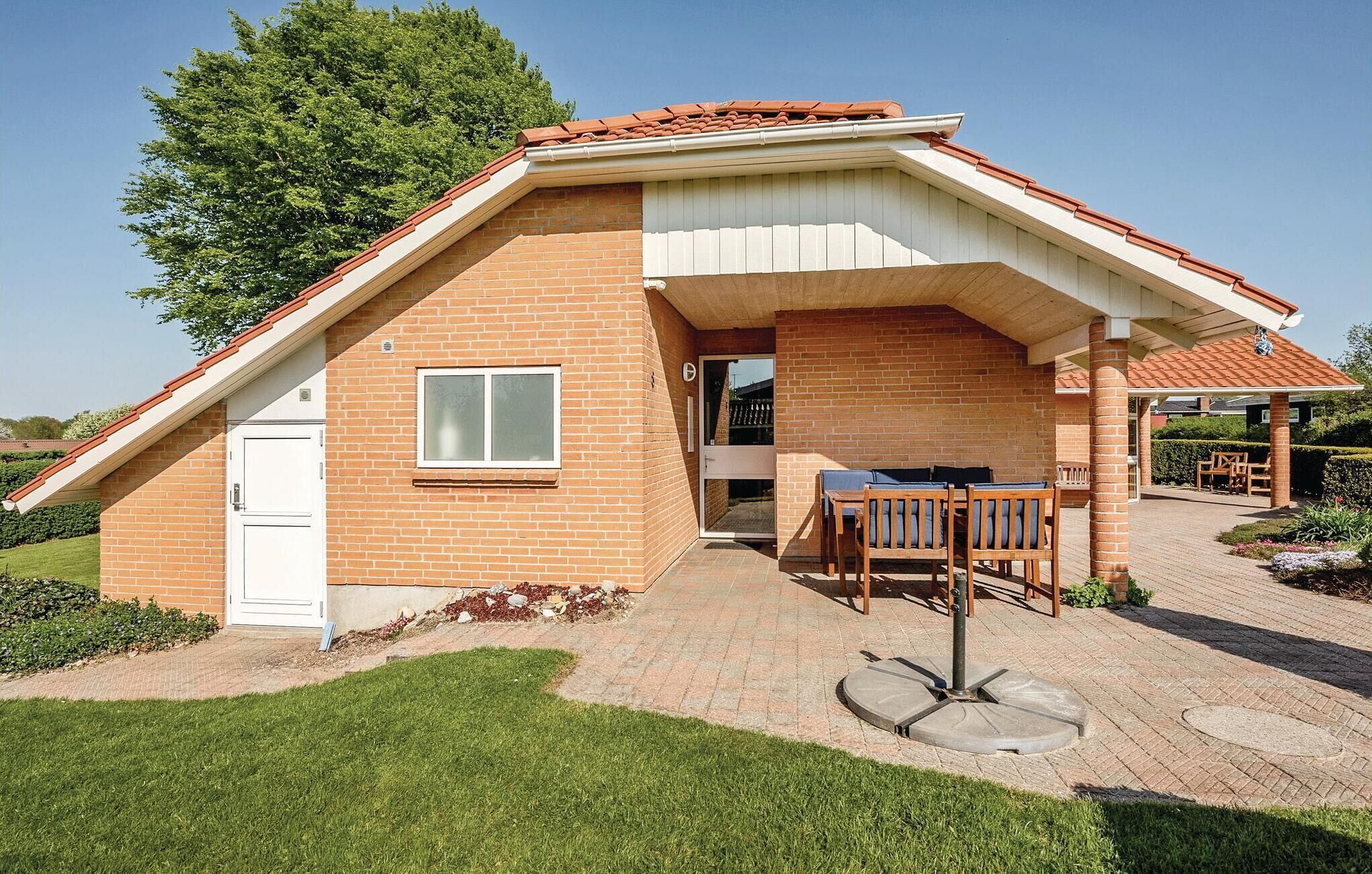 Een gelijkvloers huis met schuin dak, een voordeur en een klein terras met een tafel en stoelen.