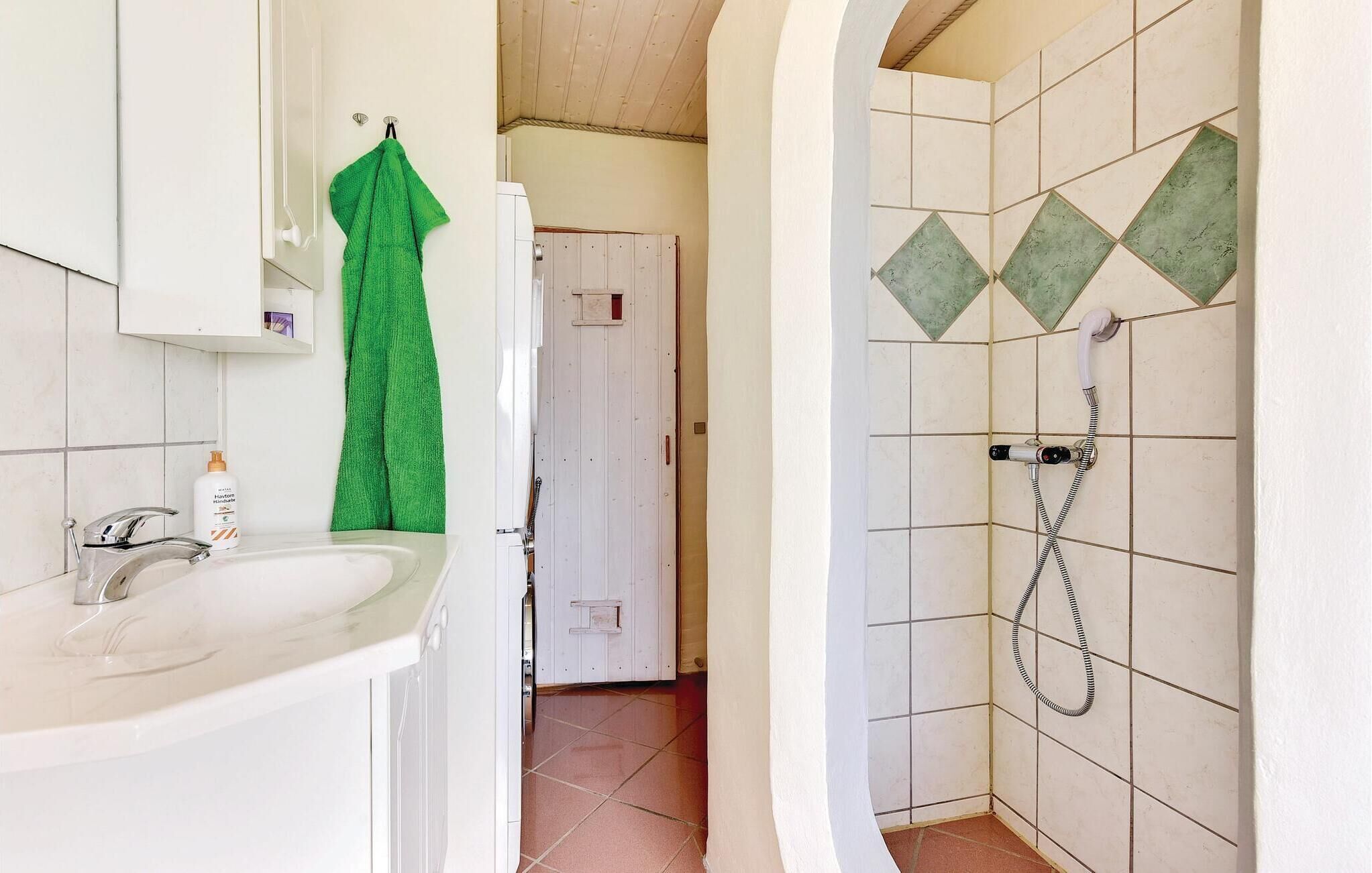 Een badkamer met een wastafel, een groene handdoek en een douche met een douchekop.