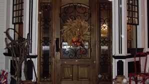 A wooden front door with a decorative wreath, a lantern above, and a red chair to the right. - Historic Hotel Broadalbin (Broadalbin)