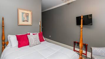 Une chambre à coucher avec un lit à baldaquin, un portrait encadré, un téléviseur à écran plat et une petite table en bois.