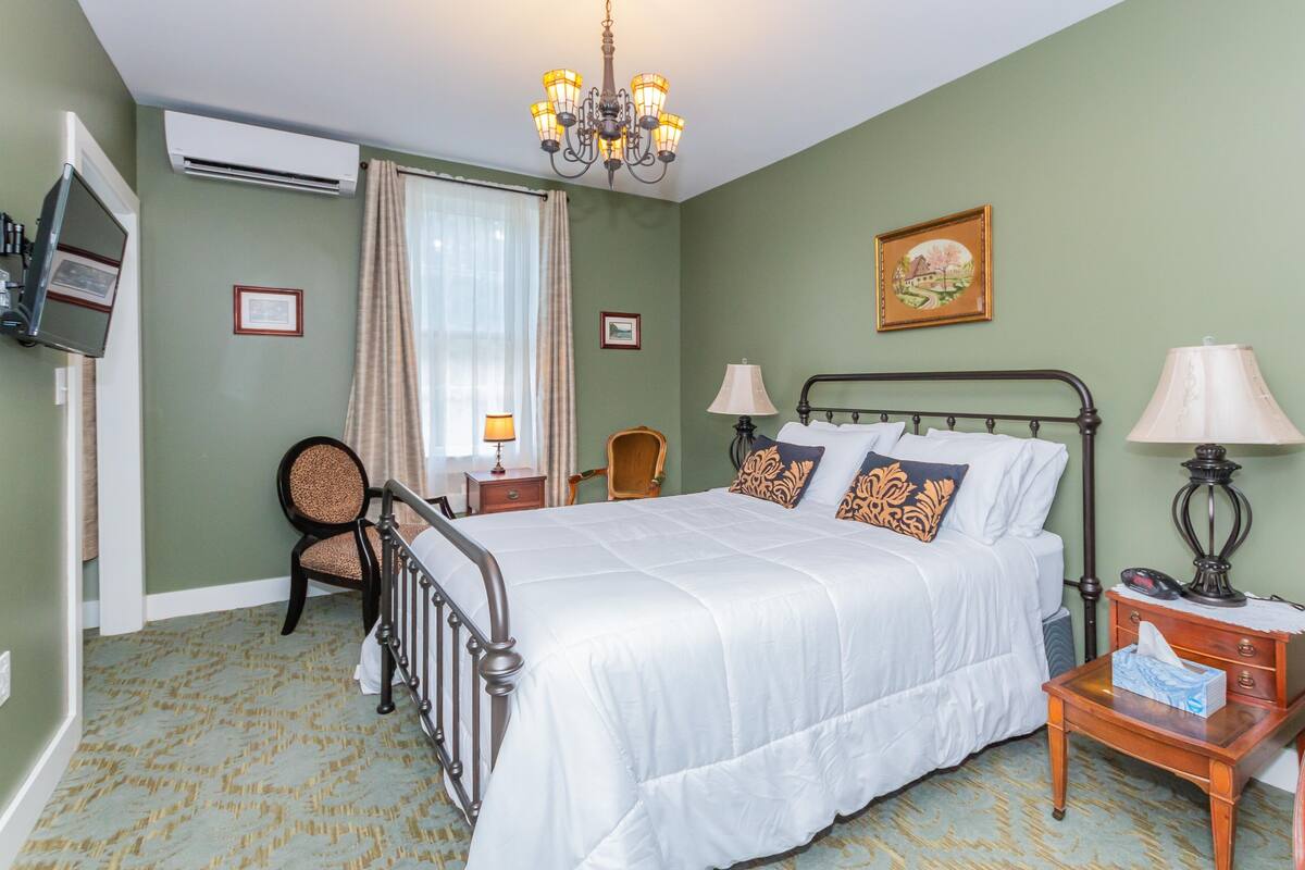 Ein Hotelzimmer mit Bett, Nachttischlampen, einem Sessel, einem Schreibtisch und einem Fernseher.