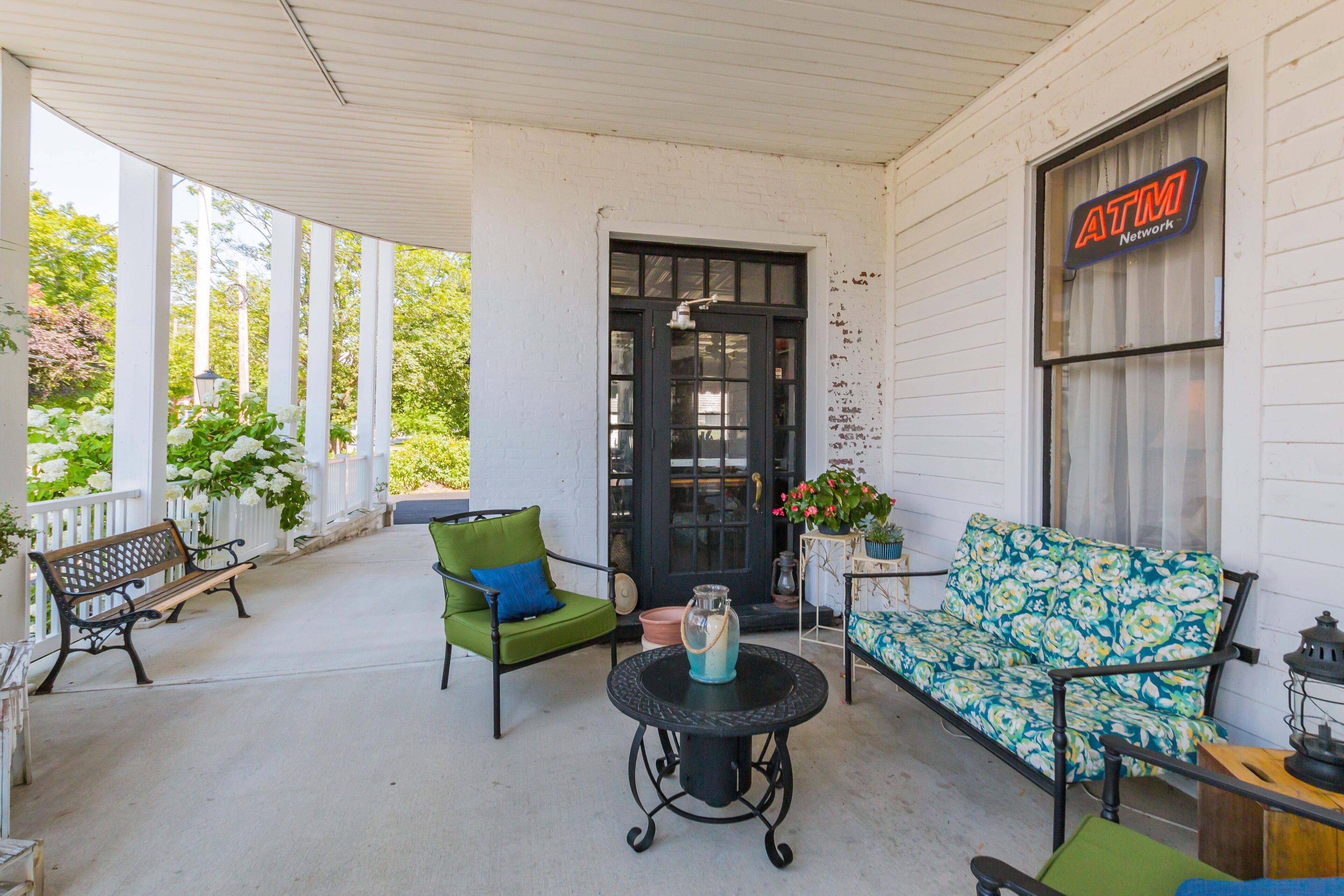 A covered porch with a bench, a table with a vase, and a sofa.