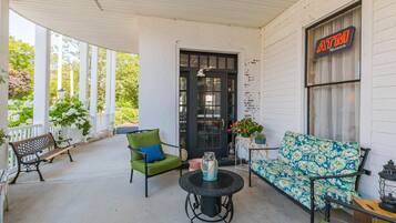 A covered porch with a bench, a table with a vase, and a sofa.