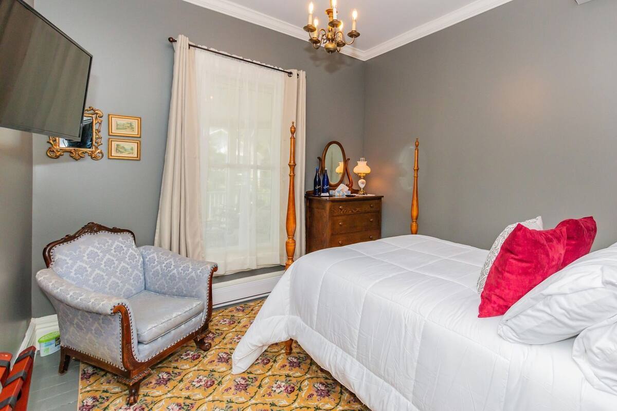 Ein Schlafzimmer mit Bett, Stuhl, Kommode, Spiegel und einer Chandelier.