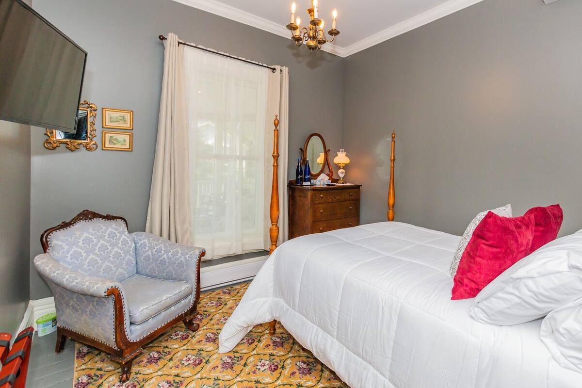 Ein Schlafzimmer mit Bett, Sessel, Schminktisch und einer Deckenleuchte.