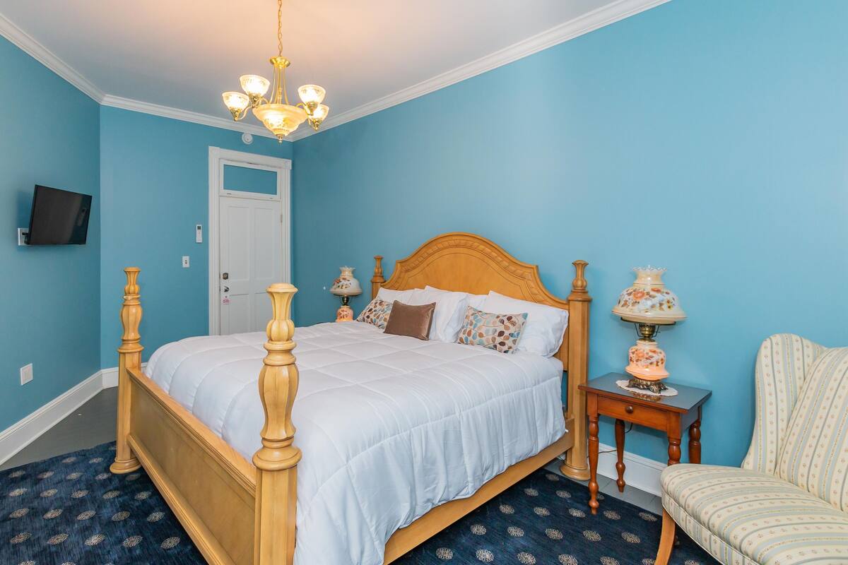 Ein Schlafzimmer mit einem hölzernen Himmelbett, einem Nachttisch mit Lampe, einem Sessel und einem an der Wand befestigten Fernseher.