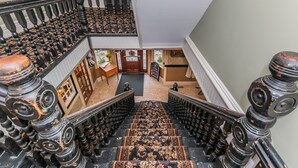 A grand staircase with ornate balusters and a patterned carpet, leading to a landing area with a door and a sign. - Historic Hotel Broadalbin (Broadalbin)