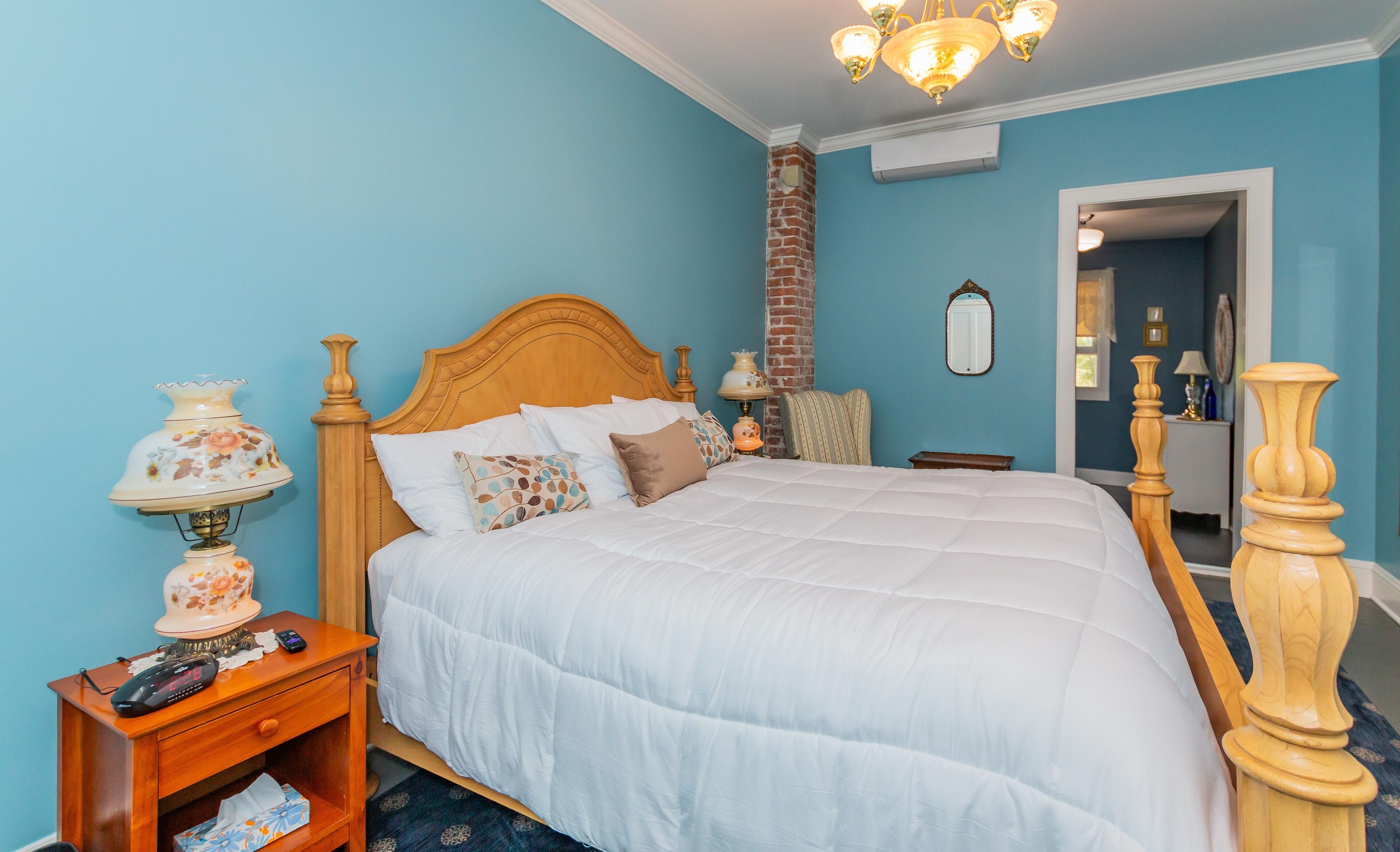 A bedroom with a wooden bed, a nightstand with a lamp, a bedside table, and a mirror on the wall.