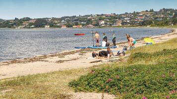 En strand med mennesker der gør sig klar til vandsport, en båd og huse i baggrunden.