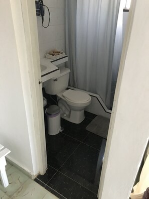 A compact bathroom with a toilet, sink, and shower, featuring a white finish and black tile flooring.