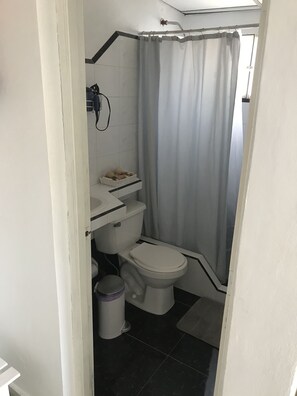 Features a white toilet, sink, and shower with a curtain, along with a dark floor and storage.