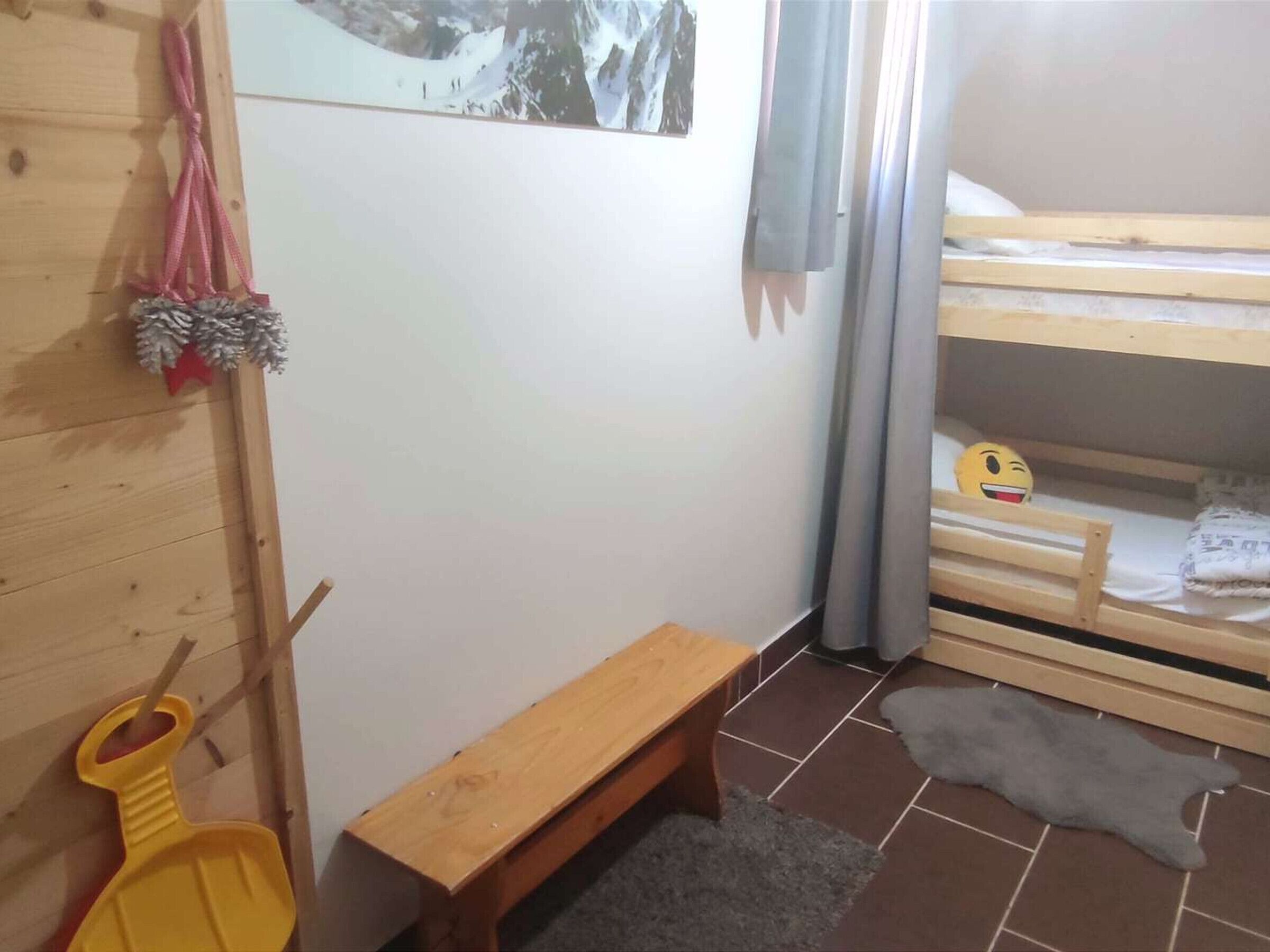 Ein Zimmer mit einem Etagenbett, einer Holzbank, einem kleinen Teppich und einem an der Wand befestigten Regal mit einem Bild und einer roten Sternverzierung.