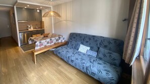 Ein gemütlicher Wohnbereich mit Küchenzeile, einer Couch mit gemustertem Bezug und einem Esstisch mit Blumenmuster-Tischdecke.