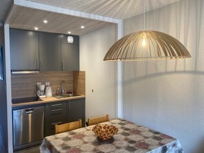 Una cocina compacta con electrodomésticos modernos, un comedor con mantel estampado e iluminación colgante.