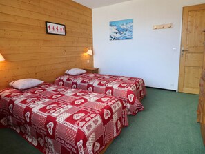 A room with two beds, wooden walls, a framed picture, a painting, and a wooden door.