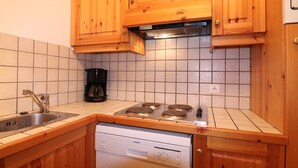 Kompakti keittiö, jossa on puukehikoiset kaapit, sisäänrakennettu liesi, astianpesukone ja kahvinkeitin.