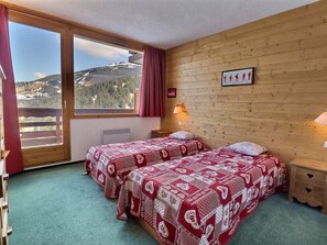 A room with two beds, a wooden wall, a window with a view of mountains, and a picture on the wall. - Charming 2-room apt for 5, pet-friendly (Méribel)
