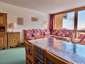 A cozy room with a wooden sofa, a dining table, and a view of the mountains through a large window. - Charming 2-room apt for 5, pet-friendly (Méribel)