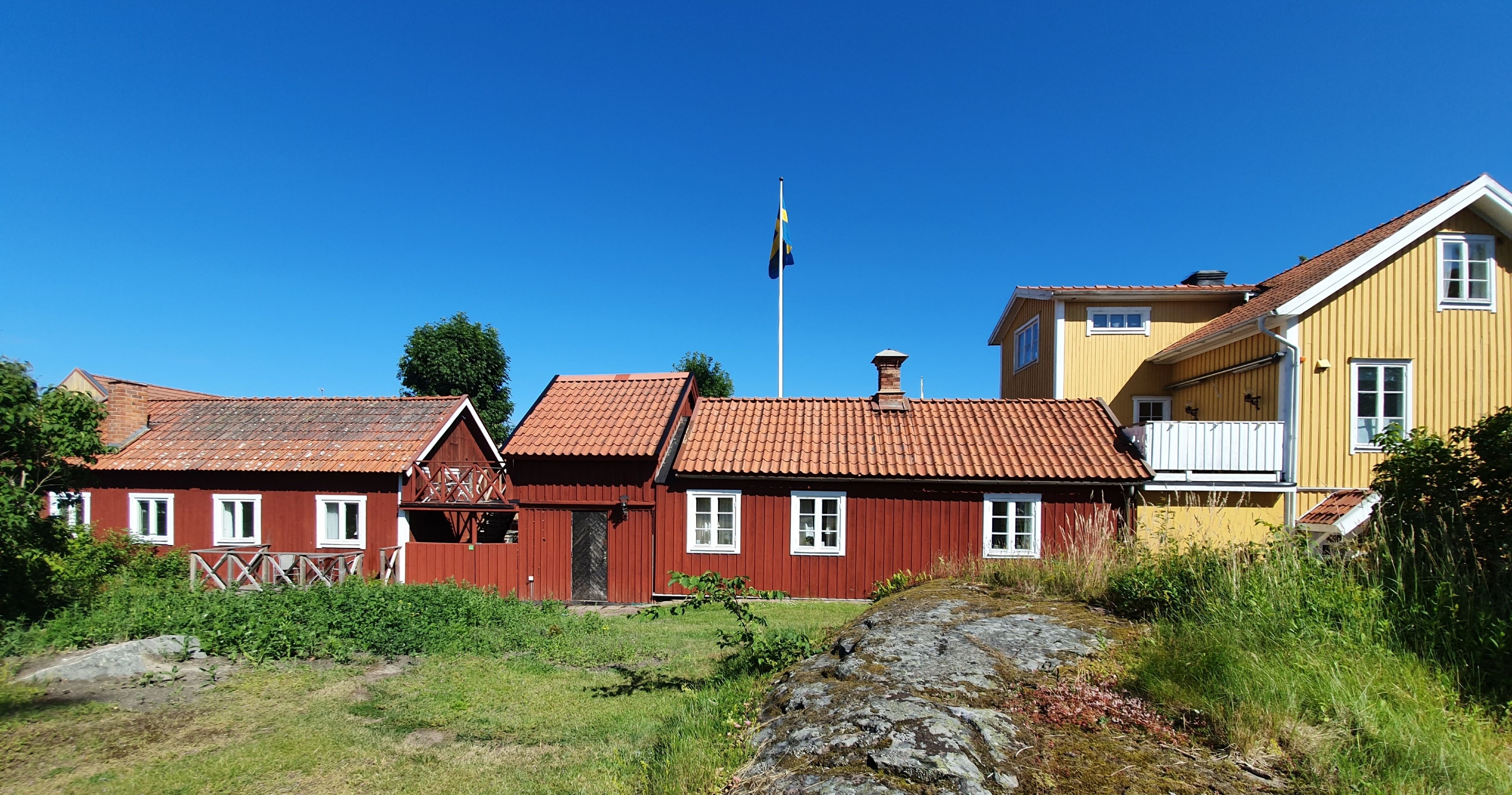 Une rangée de maisons traditionnelles aux couleurs rouge et jaune, avec un mât sur lequel flotte un drapeau au centre.