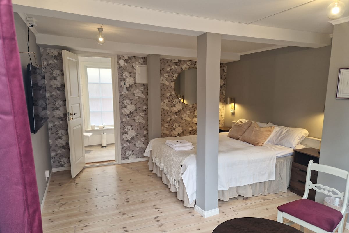 A bedroom with a bed, a chair, a bedside table, a lamp, and a window.