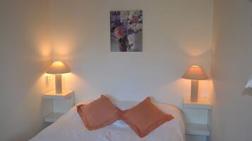 A neatly made bed with two pillows, two bedside lamps, and a framed floral artwork on the wall.