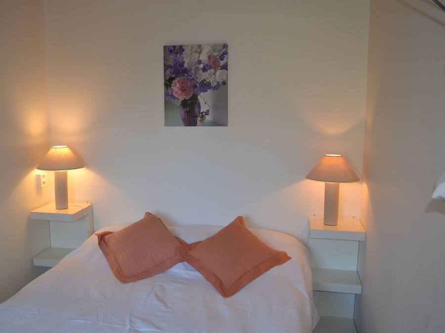 A neatly made bed with two pillows, two bedside lamps, and a framed floral artwork on the wall.