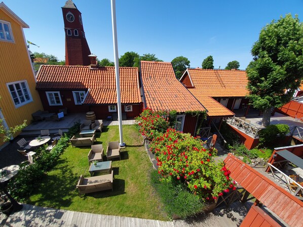 A courtyard with outdoor seating, a clock tower, and a red-roofed building. - Hotell Klockargården (Öregrund)