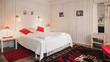 Une chambre à coucher bien rangée, avec un grand lit, un tapis à motifs rouges et blancs, et une commode blanche avec un miroir.