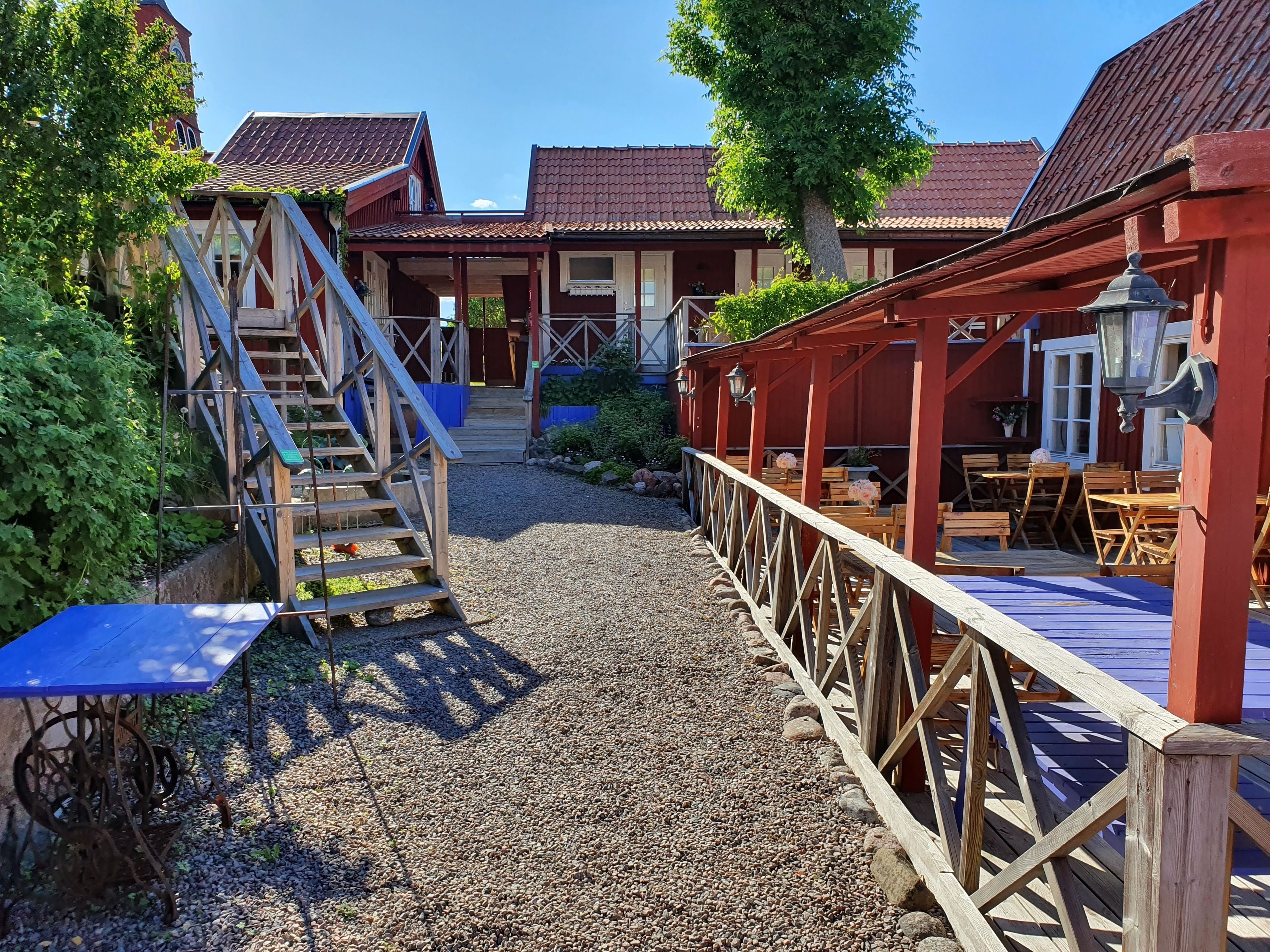 Un bâtiment rustique en bois, avec un chemin de gravier menant à un espace extérieur abrité, aménagé pour s’asseoir.