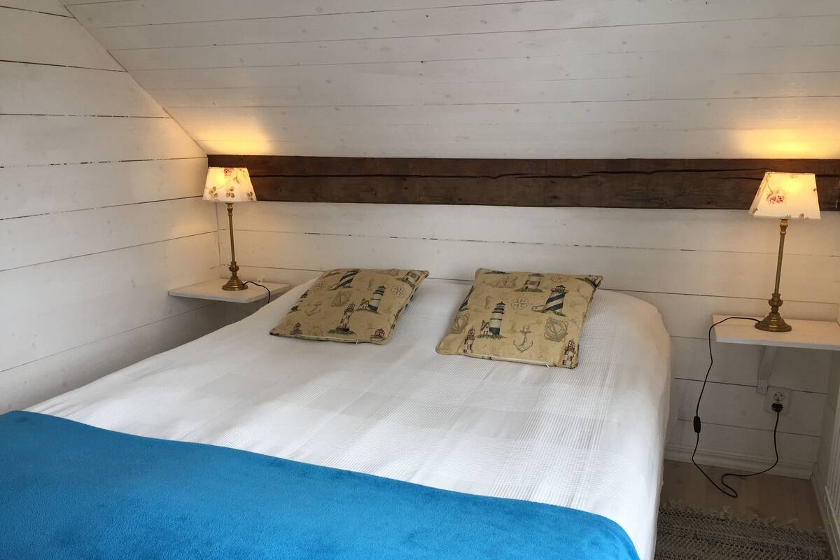 A room with a bed, two nightstands, two lamps, a blue blanket, and a patterned pillow.