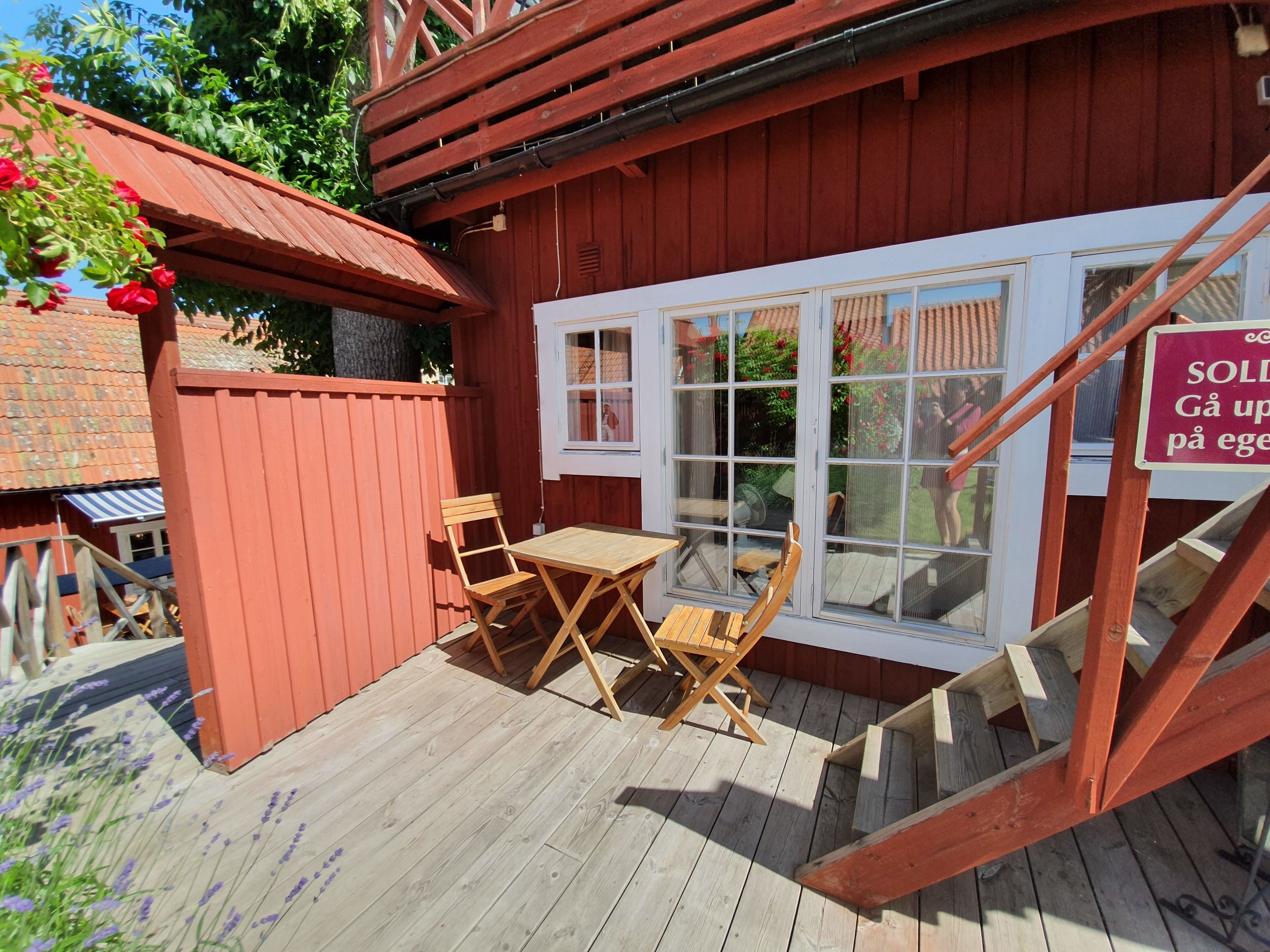 Eine Holzterrasse mit Tisch und Stühlen, ein roter Holzzaun und ein Fenster mit einem Schild.