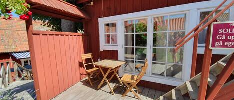 Eine Holzterrasse mit Tisch und Stühlen, ein roter Holzzaun und ein Fenster mit einem Schild.