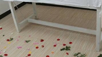Una mesa blanca con mantel floral, rodeada de pétalos de rosa dispersos sobre un suelo de madera.