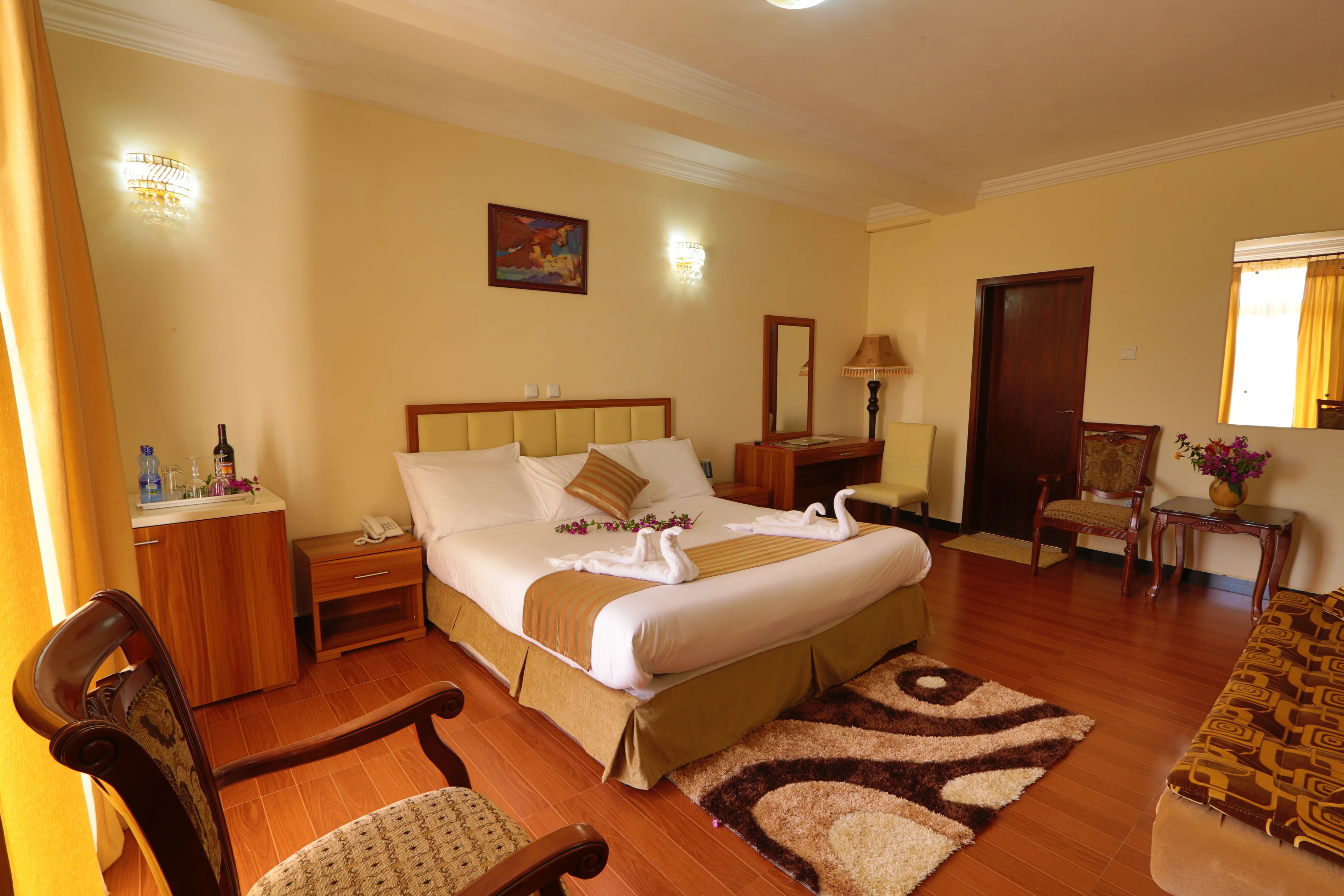 A hotel room with a large bed, bedside tables, a chair, a desk, and a small table with a vase of flowers.