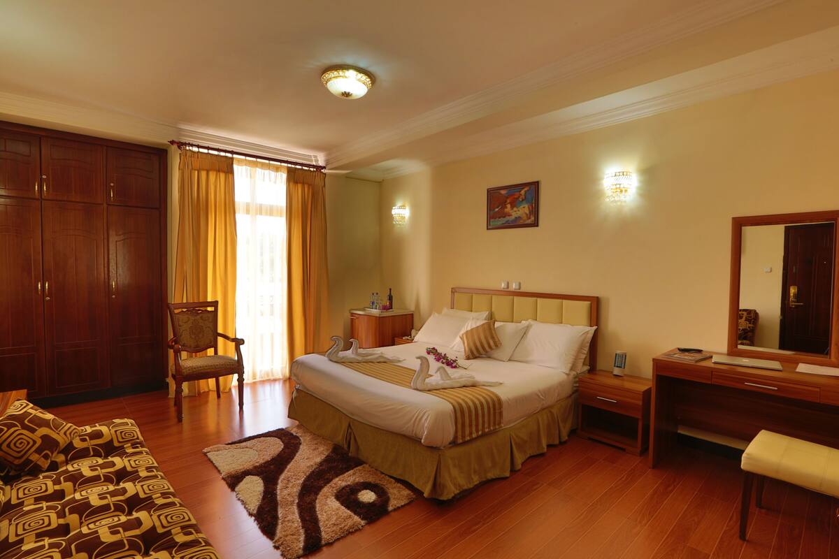 Una habitación de hotel con cama, escritorio, silla, armario y sofá.