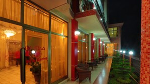 A hotel exterior at night with glass doors, red pillars, outdoor seating, and a well-lit pathway. - Bete Daniel Hotel (Bahir Dar)