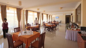 A dining area with tables set for service, a buffet line, and a staff member present. - Bete Daniel Hotel (Bahir Dar)