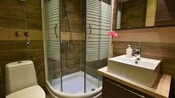 A modern bathroom with a glass-enclosed shower, a white toilet, and a sink with a soap dispenser.