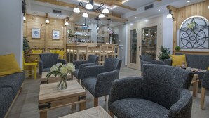 Un interior moderno con vigas de madera en el techo, sillas tapizadas en gris, una mesa de madera con un florero y una zona de bar con estanterías y cristalería.